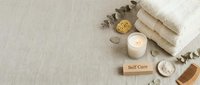 Soft self care flat lay with folded towels, lit candle, wooden comb, sea salt, sponge, and eucalyptus on linen background with copy space.