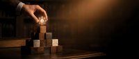 Hand placing glowing lightbulb on top of wooden block pyramid, symbolizing innovation, business growth, and strategic planning for corporate success.