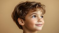 Young boy with wavy brown hair and bright eyes looking up with hopeful expression against warm beige background, conveying innocence and wonder.