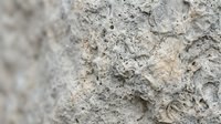 Rough textured concrete wall surface with natural weathering and erosion patterns showing aggregate stones and porous cement material.