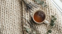 Herbal tea cup with dried lavender sprigs and eucalyptus leaves on chunky knit blanket creating cozy aromatherapy wellness scene for relaxation and self-care.
