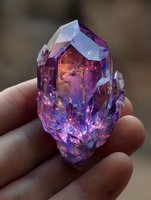 Vibrant purple and blue crystal cluster held between fingers, showcasing iridescent reflections and faceted surfaces for jewelry design or spiritual healing.
