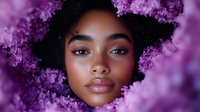 Young African American woman with natural curly hair surrounded by purple flowers creating dreamy spring portrait with soft bokeh lighting effects and romantic atmosphere.