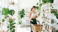 Woman in athletic wear shopping for skincare and wellness products in a bright, plant-filled store with shelves of cosmetics and natural beauty items.