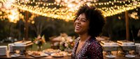 Happy African American woman laughing at outdoor dinner party with string lights and elegant table setting during golden hour celebration.