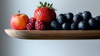 Fresh mixed berries and apple arranged on wooden serving board against neutral background, showcasing vibrant colors and natural textures for food photography.