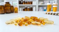 Various vitamin and supplement capsules scattered on white surface with pharmacy bottles in blurred background for healthcare and wellness concepts.