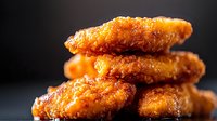 Crispy golden chicken nuggets stacked in pileicy meat on dark background, macro food photography with selective focus.
