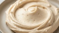 Creamy whipped frosting or mousse swirled in a white bowl, showcasing smooth texture and rich consistency for baking, dessert, and culinary design projects.