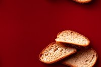 Fresh crusty baguette slices arranged on deep red background showing detailed bread texture and air holes, minimalist food photography composition.