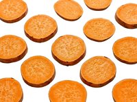 Sliced sweet potato rounds arranged in rows on white background, showing vibrant orange flesh texture for food and nutrition content.