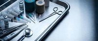 Medical instruments and supplies arranged on sterile steel tray including syringes, scissors, stethoscope and vials for healthcare procedures.
