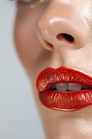 Close-up of glossy red lips and nose on light skin with natural makeup. Macro beauty shot showing detailed texture and shine of lipstick application.