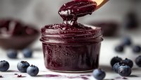 Homemade blueberry jam in glass jar with wooden spoon and fresh berries on kitchen counter for breakfast and cooking recipes.