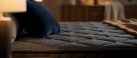 Cozy bedroom scene with navy blue pillow on quilted gray bedding, warm ambient lighting, and soft furnishings creating a relaxing sleep environment for home decor and lifestyle content.
