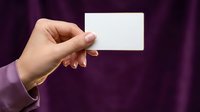 Woman's hand holding blank white business card against purple background, mockup for branding, identity, and marketing design.