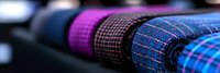 Colorful plaid and checkered fabric rolls in textile store showcase, macro close-up view with selective focus showing texture and pattern details.