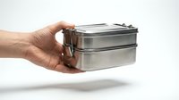 Hand holding a stainless steel two-tier lunch box isolated on white background, eco-friendly reusable food container for meal prep.