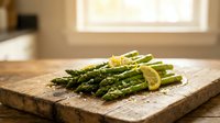Fresh green asparagus spears with lemon slices on rustic wooden cutting board in bright kitchen setting for healthy cooking and meal preparation.