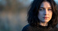 Young brunette woman with wavy hair wearing knit sweater in soft natural light. Contemplative expression with warm golden hour lighting for lifestyle content.