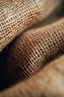 Natural burlap fabric close-up showing detailed woven texture and fibers in warm brown tones, suitable for rustic design backgrounds and organic product packaging.