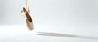Single ballet pointe shoe hanging from ribbon against clean white background, elegant dance footwear for performance and training studio use.