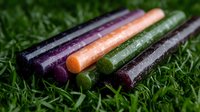 Colorful fruit leather strips with natural ingredients lying on green grass. Healthy snacks made from pureed fruits and vegetables, covered in water drops.