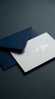 Elegant thank you card with silver foil calligraphy resting on a navy blue envelope against a dark background.