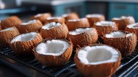 Halved coconuts with white flesh displayed on dark surface, ready for culinary use, food preparation, tropical ingredients, and cooking content.