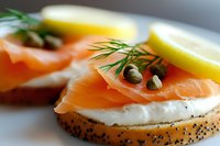 Fresh smoked salmon and cream cheese on poppy seed bagel with capers, dill garnish and lemon wedge, macro food photography for restaurant menu.