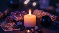 Mystical fortune telling setup with burning candle, tarot cards, crystal ball and gemstones creating atmospheric divination scene for spiritual guidance.
