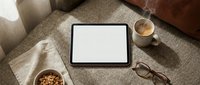 Blank tablet screen with coffee cup and glasses on cozy sofa for digital mockup presentations and app development showcasing.