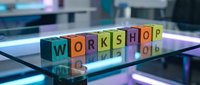 Colorful wooden letter blocks spelling WORKSHOP on reflective glass surface in modern office environment for business training and education concepts.