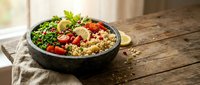 Healthy quinoa bowl with fresh vegetables, cherry tomatoes, herbs and lemon on rustic wooden table. Nutritious meal for clean eating and wellness lifestyle.