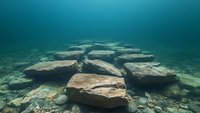Underwater landscape with large flat rocks scattered across sandy bottom in turquoise waters, creating natural stepping stones in mysterious marine environment.