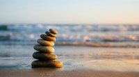 Balanced stone stack on sandy beach at sunset with gentle ocean waves creating peaceful zen meditation atmosphere for wellness and mindfulness practices.