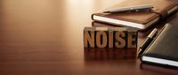 Wooden letter blocks spelling NOISE on desk with notebooks and pen in warm office lighting for communication and sound concepts.