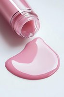Pink liquid cosmetic product spilling from bottle creating smooth glossy puddle on white surface, close-up view for beauty and skincare advertising.