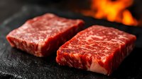 Fresh raw marbled beef steaks on dark stone surface with fire flames in background, close up view showing meat texture and premium quality.