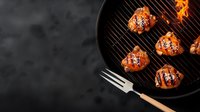 Grilled chicken wings with sesame seeds on black round barbecue grill. Orange-glazed poultry pieces cooking on dark background with copy space. Food photography.