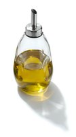 Glass oil dispenser bottle with golden olive oil and stainless steel pouring spout isolated on white background for kitchen and cooking applications.