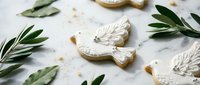 White dove-shaped cookies with intricate icing details surrounded by olive branches on marble surface for peace celebrations and religious holidays.