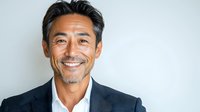 Confident mature Asian businessman with genuine smile wearing dark suit and white shirt against light background, professional corporate portrait.