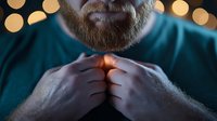Close up portrait of mature bearded man in teal sweater adjusting collar against blurred golden bokeh lights background, creating cozy winter atmosphere.