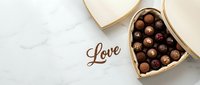 Heart-shaped box of assorted chocolate truffles on marble surface with Love inscription, romantic Valentine's Day gift concept.