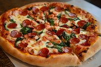 Fresh baked pizza with melted mozzarella cheese, crispy pepperoni slices, and spinach leaves on golden crust, close-up view showing texture and toppings.