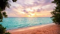 Tropical beach at sunset with turquoise water, golden sky, and lush vegetation framing the shore, ideal for travel and vacation marketing.
