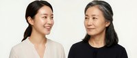 Asian mother and adult daughter smiling together in casual clothing against neutral background for family bonding and generational relationship concepts.