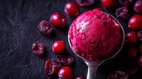 Vibrant scoop of cranberry sorbet garnished with fresh and dried cranberries on dark slate background, showcasing rich burgundy color and smooth texture.