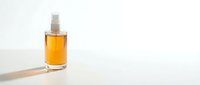 Amber glass bottle with spray pump containing golden liquid cosmetic product on white surface with soft natural lighting and minimalist background for skincare branding.